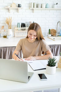Young woman using phone while sitting on table