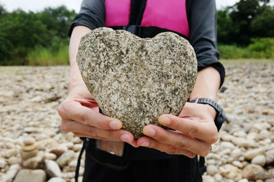 Midsection of woman holding heart shape rock at beach