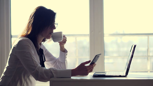 A female clerk office worker browses social networks on a mobile phone during her short coffee break