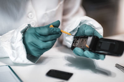 Midsection of detective repairing mobile phone on table