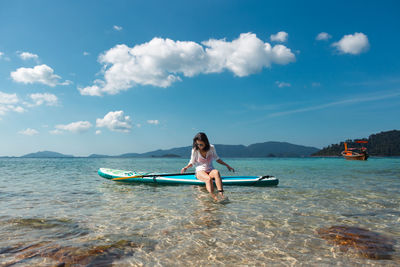 Woman sitting on the paddleboard in sea against sky