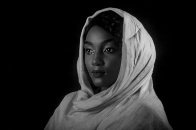 Close-up of young woman in hijab against black background