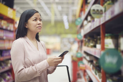 Woman looking at prices during inflation while doing shopping in supermarket