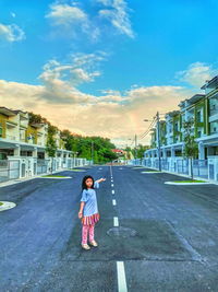 Full length of a girl standing on road in city against sky