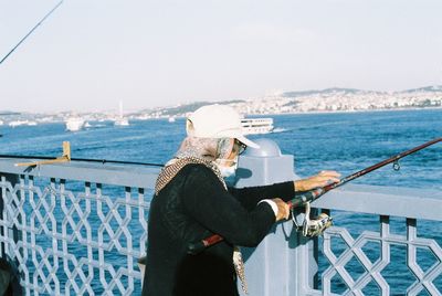 Man standing on railing by sea against sky