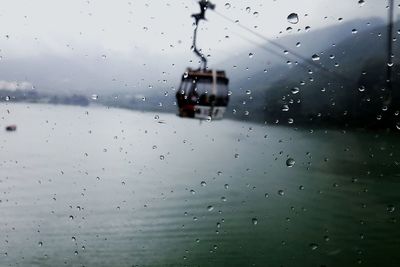 Overhead cable car over lake seen through wet glass window