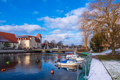 Boats moored in canal by buildings against sky