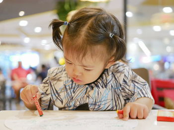 Cute baby girl coloring paper at table in restaurant