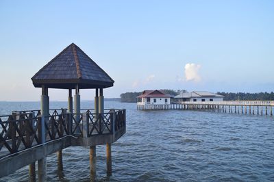 Stilt house on sea by building against sky