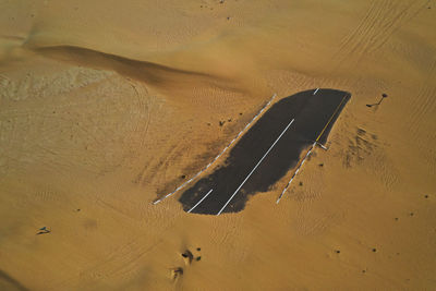Drone shot of an asphalt road covered in sand in the desert.