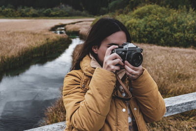 Portrait of young woman taking photos of autumn nature with vintage camera