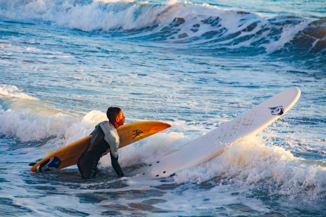 REAR VIEW OF MAN SURFING IN SEA