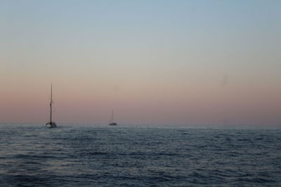 Sailboat sailing in sea against clear sky during sunset