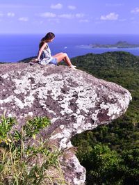 Woman sitting on rock by sea against sky