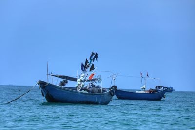 Fishing boat sailing in sea against clear blue sky