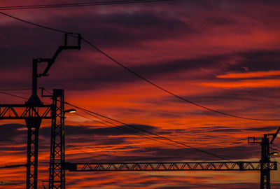 Low angle view of silhouette electricity pylon against orange sky