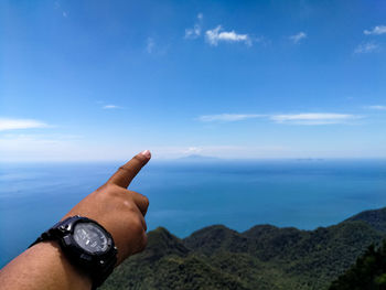 Close-up of hand by sea against sky