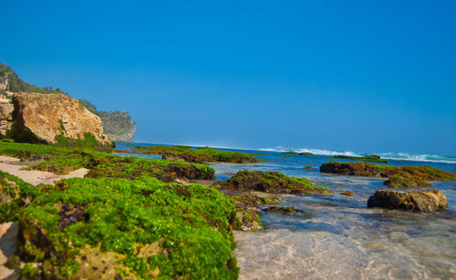 Rocks by sea against clear blue sky