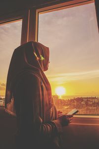 Side view of woman holding smart phone by window