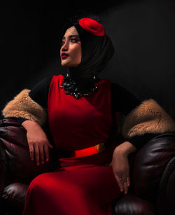 Young woman looking away while sitting against black background