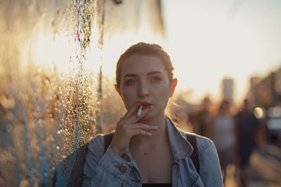 Young woman smoking while standing by wall in city