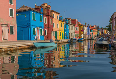 Boats moored in canal by houses against sky