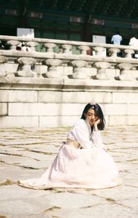 Side view of young woman in dress crouching on footpath during sunny day