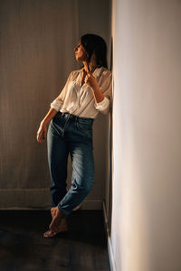 Woman looking at camera while standing against wall at home