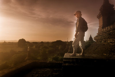 Side view of man standing on old ruin at sunset