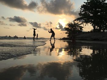 Silhouette people on beach against sky during sunset