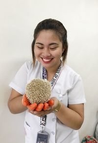 Young woman holding hedgehog while standing against wall