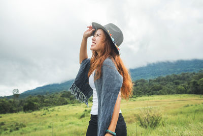 Side view of smiling woman wearing hat standing on field against sky