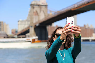 Woman taking selfie against bridge in city