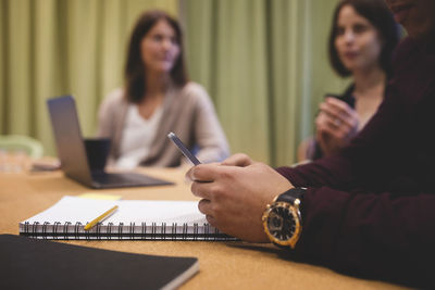 Close-up of businessman using phone at conference table with colleagues in background