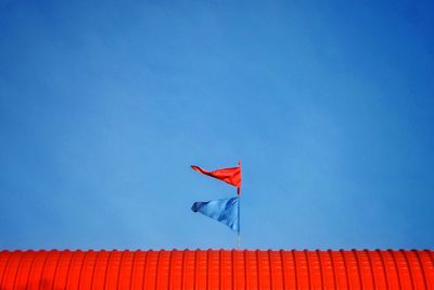 Low angle view of flags on red roof against blue sky