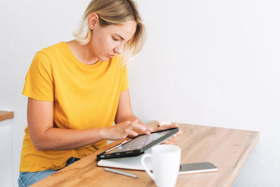 Young woman studies cryptocurrency charts and stock quotes on digital tablet with cup of tea at home