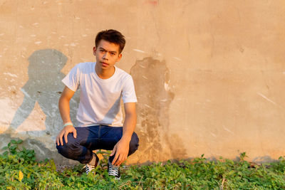 Full length of young man sitting against wall