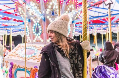 Thoughtful young woman sitting on illuminated carousel at night