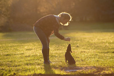 Side view of woman playing with dog on field during sunset