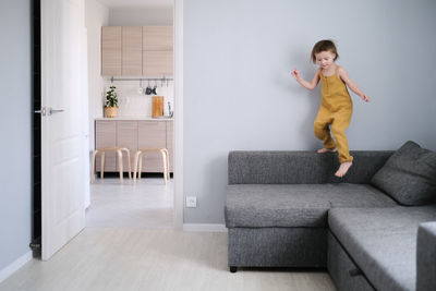 Child jumps and plays on sofa in minimalist living room, gray sofa.