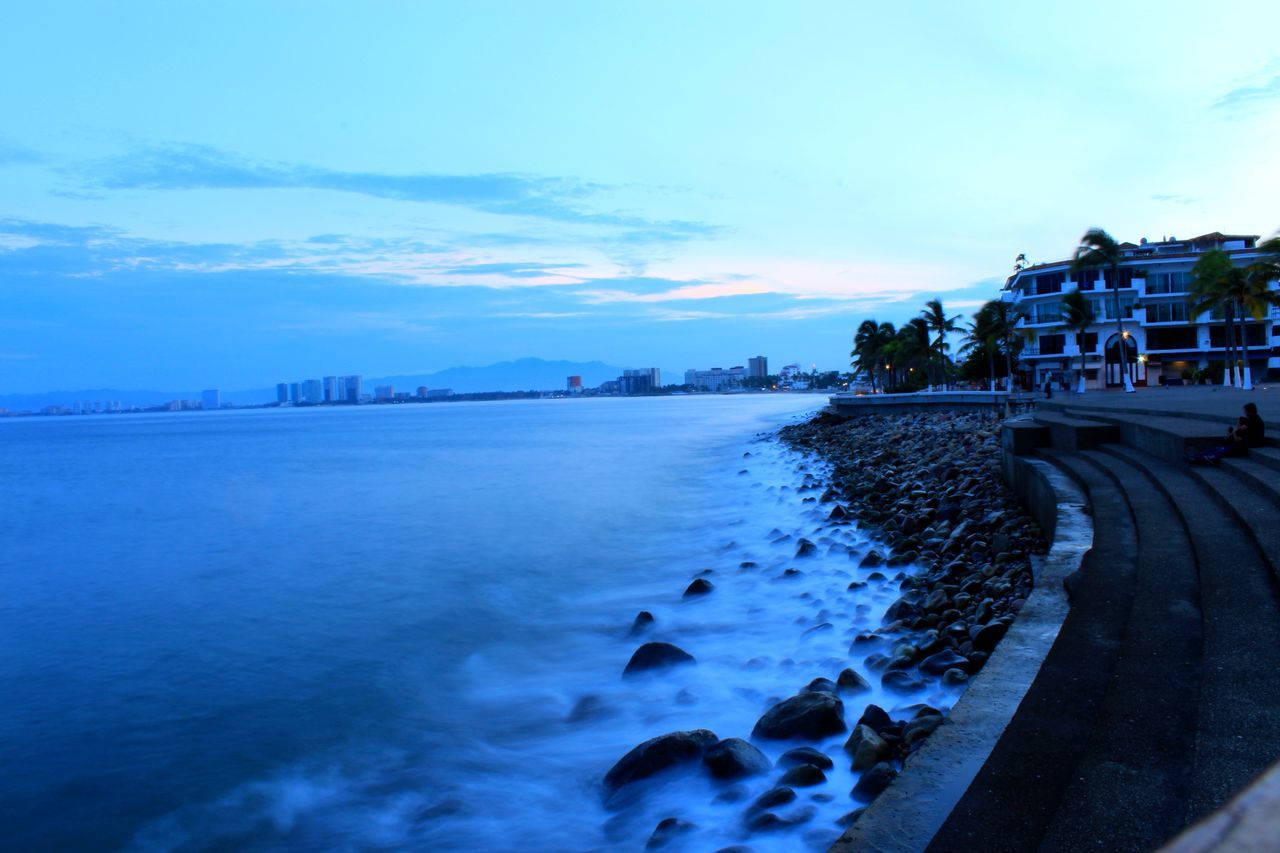 building exterior, architecture, built structure, water, city, sky, tranquil scene, blue, tranquility, scenics, sea, waterfront, shore, nature, day, outdoors, residential district, remote, cloud - sky, beauty in nature, coastline, city life, no people