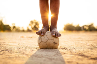 Low section of person with soccer ball on field during sunset