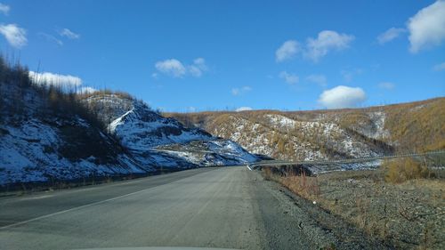 Empty road by snowcapped mountains against sky