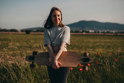 Portrait of an ordinary teen girl from the village. the girl holds a longboard in a hand and smiles