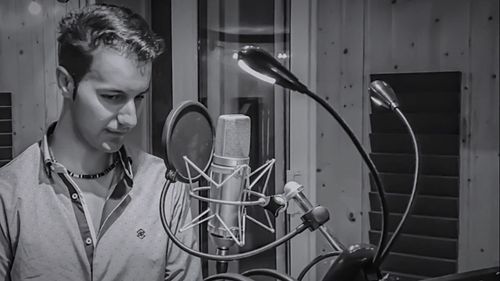 Young man standing by microphone in recording studio