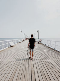 Rear view of man standing on pier over sea against clear sky