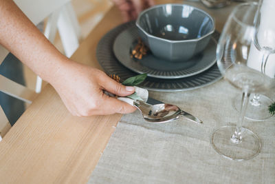 Young woman in the plaid shirt sets festive table with fir composition, christmas time