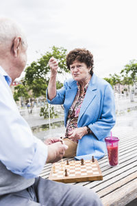 Portrait of senior woman sitting on a bench playing chess with her husband