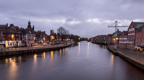 River amidst illuminated buildings in city against sky