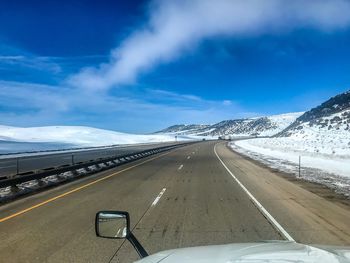 Road amidst snowcapped mountains against sky seen through car windshield